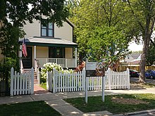 Pale yellow wooden house with brown trim surrounded by white picket fence